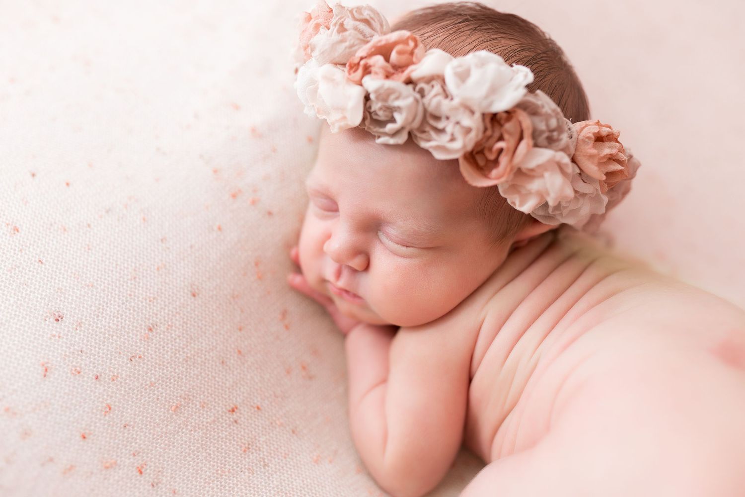 Newborn baby lying on soft pink and white floral backdrop during professional photo session.