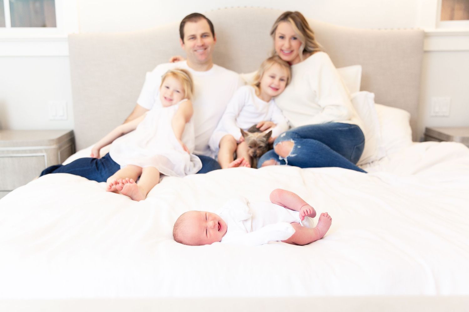 Family members relaxing together on a comfortable white bed in casual attire.