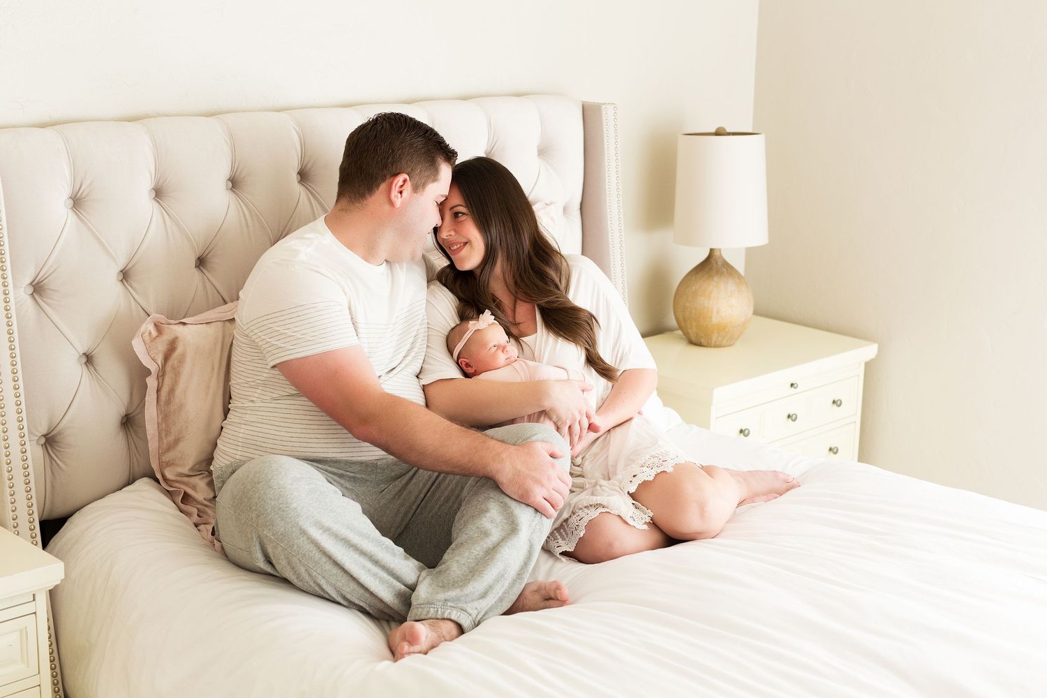 Intimate family moment on a white tufted headboard bed with neutral decor and gold accents.