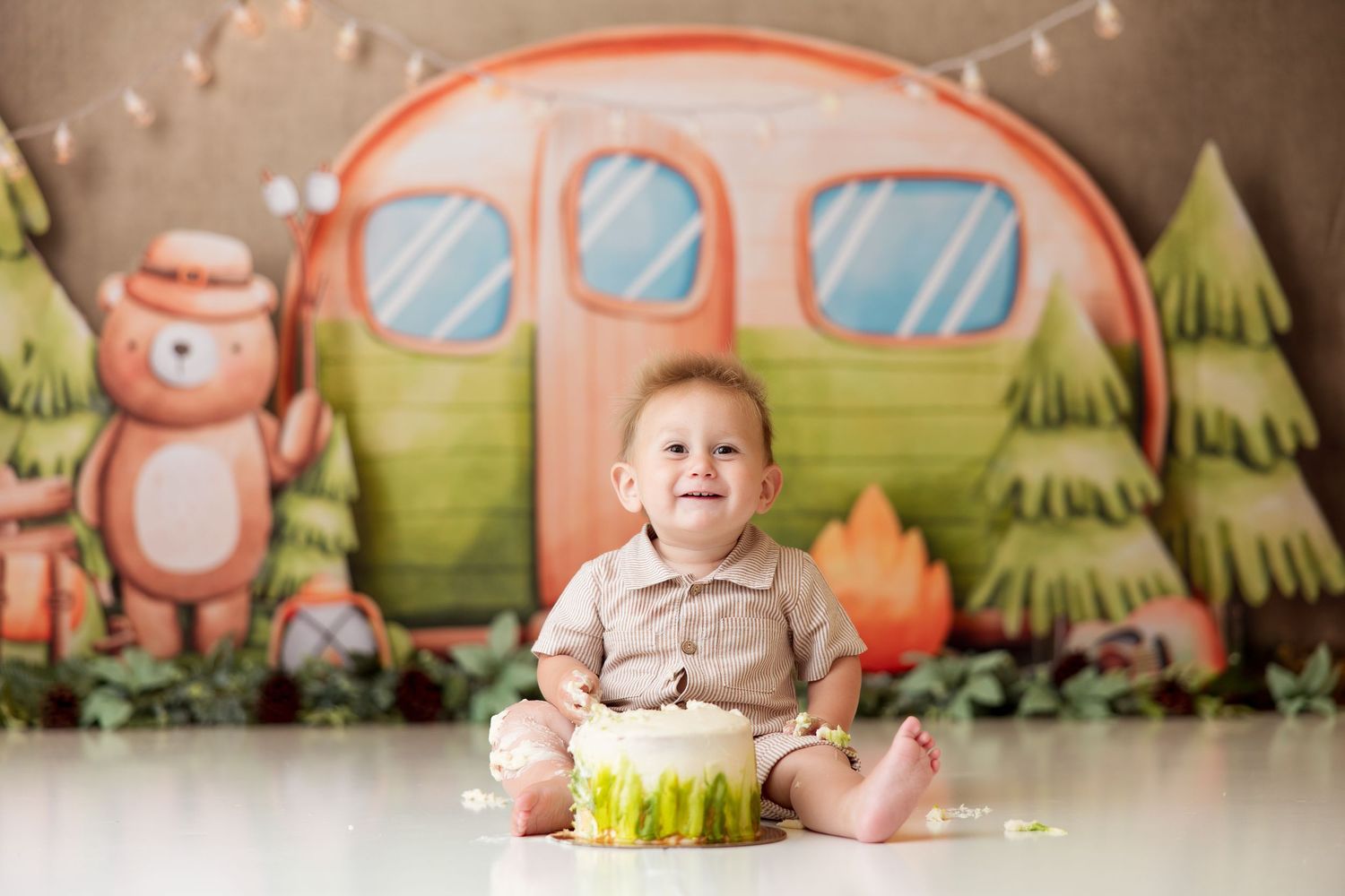 Whimsical camping-themed backdrop with pink camper and string lights for baby photography.