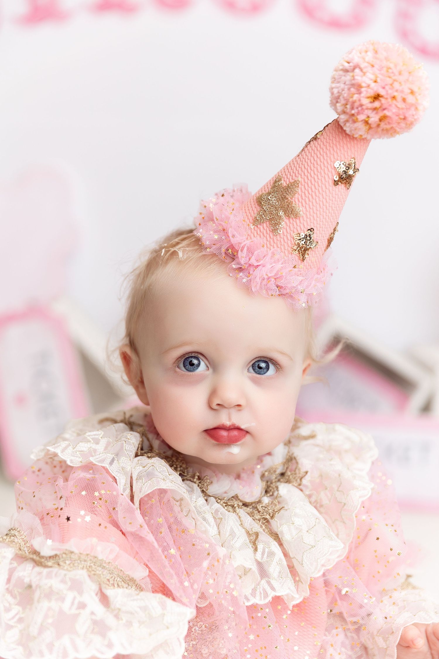 Whimsical portrait with baby wearing pink party hat with gold stars and lace dress.