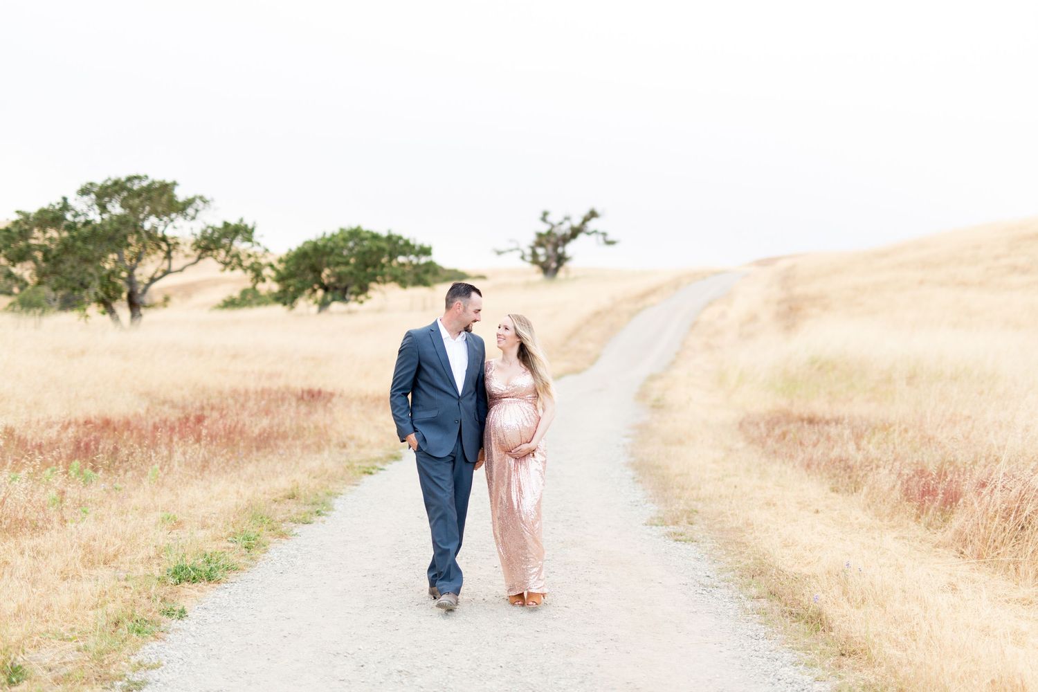 Family walking together on a scenic dirt path through golden rolling hills at sunset.