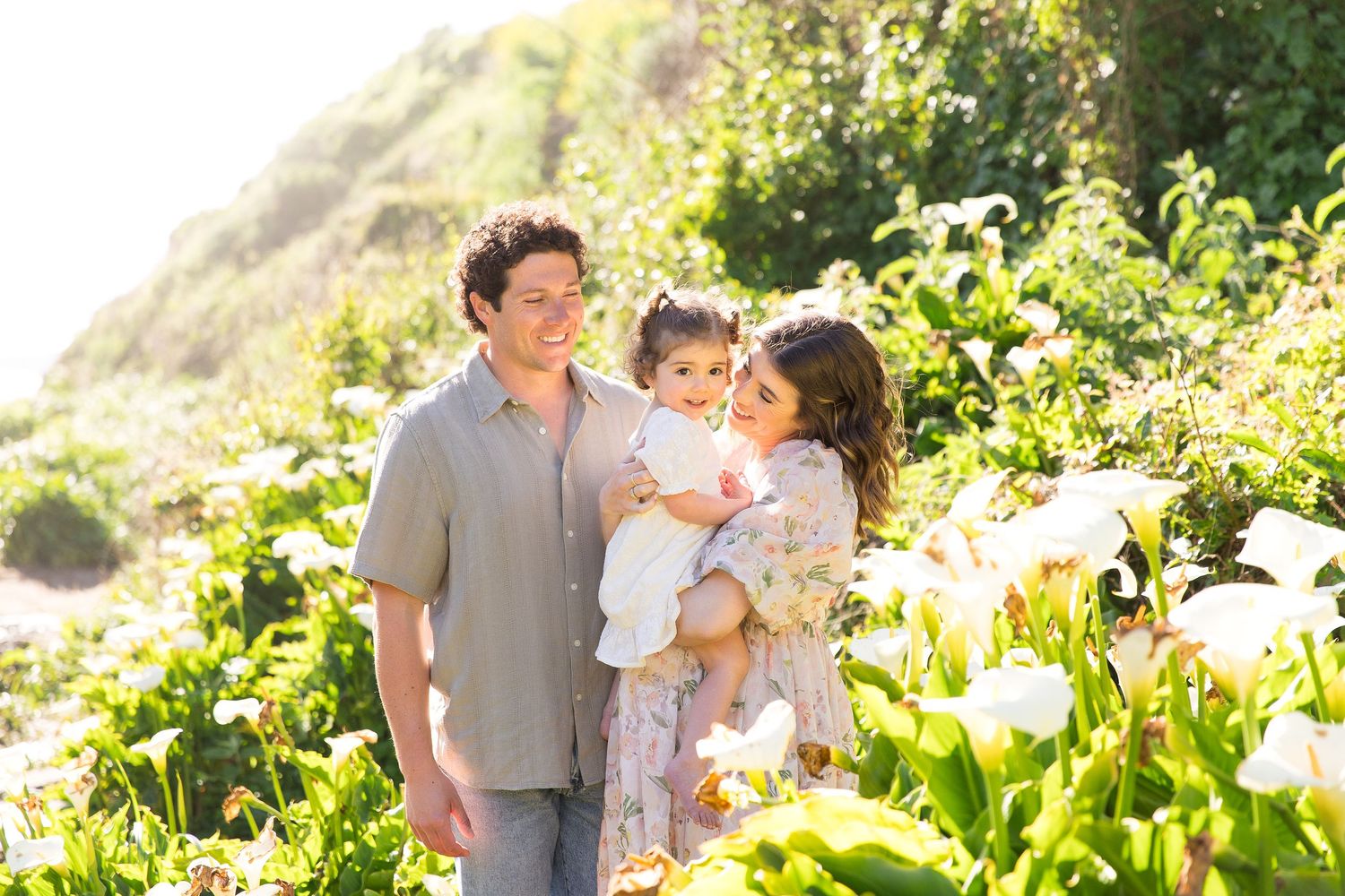 Family enjoying a tender moment among blooming calla lilies by the coast.
