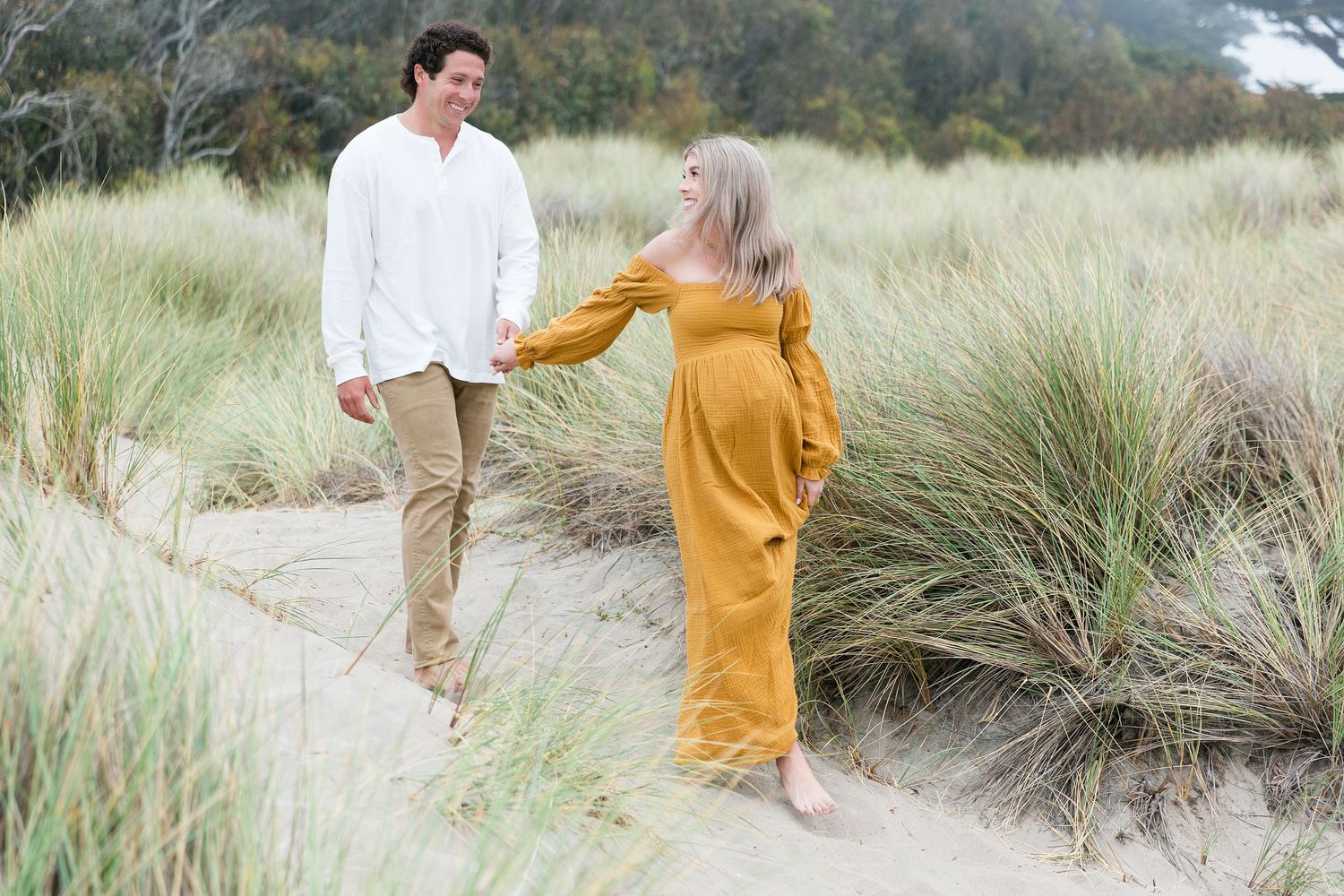 Couple walking through tall beach grass during golden hour photoshoot.