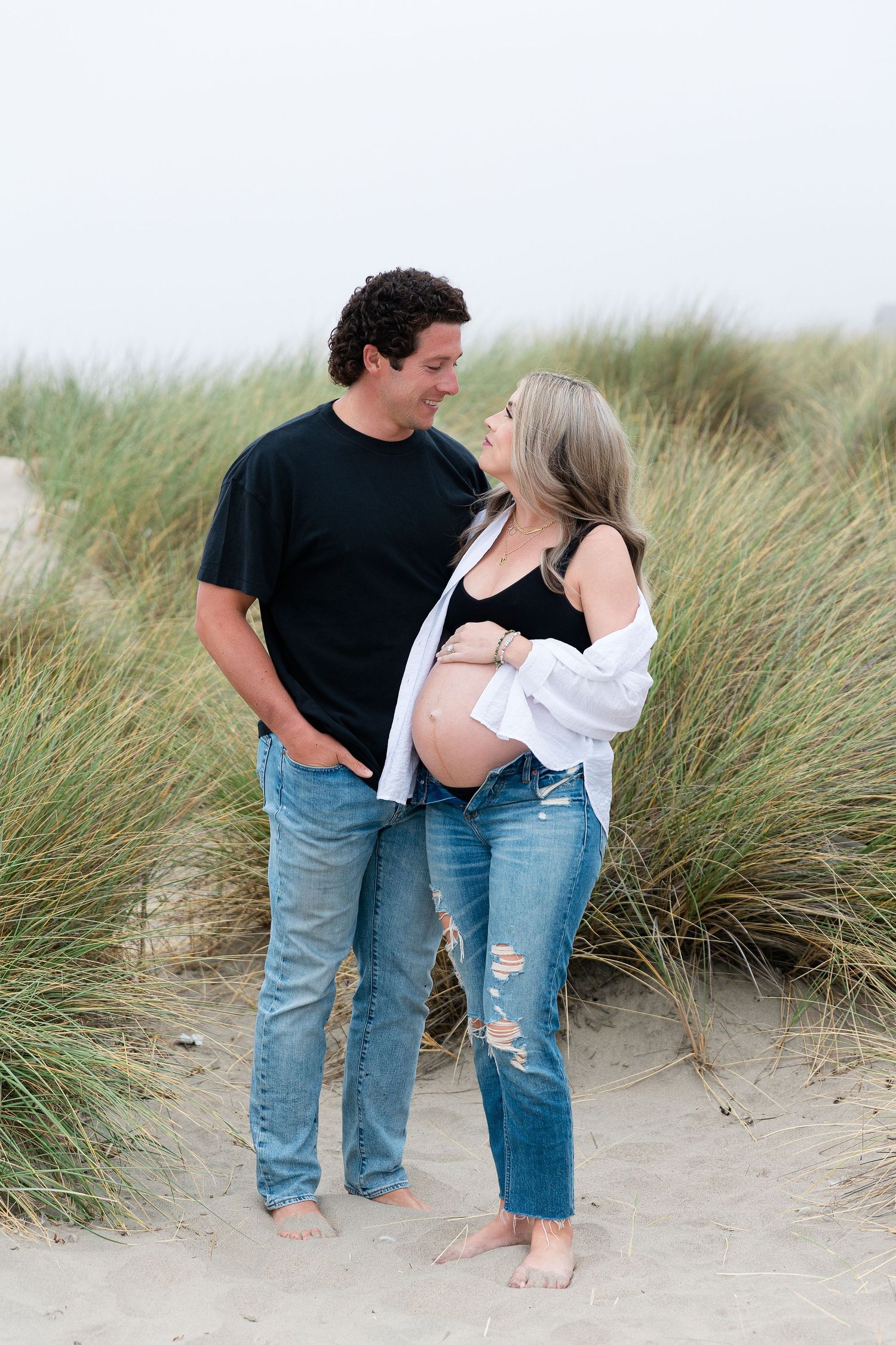 Romantic couple's maternity photo on beach with coastal grasses.