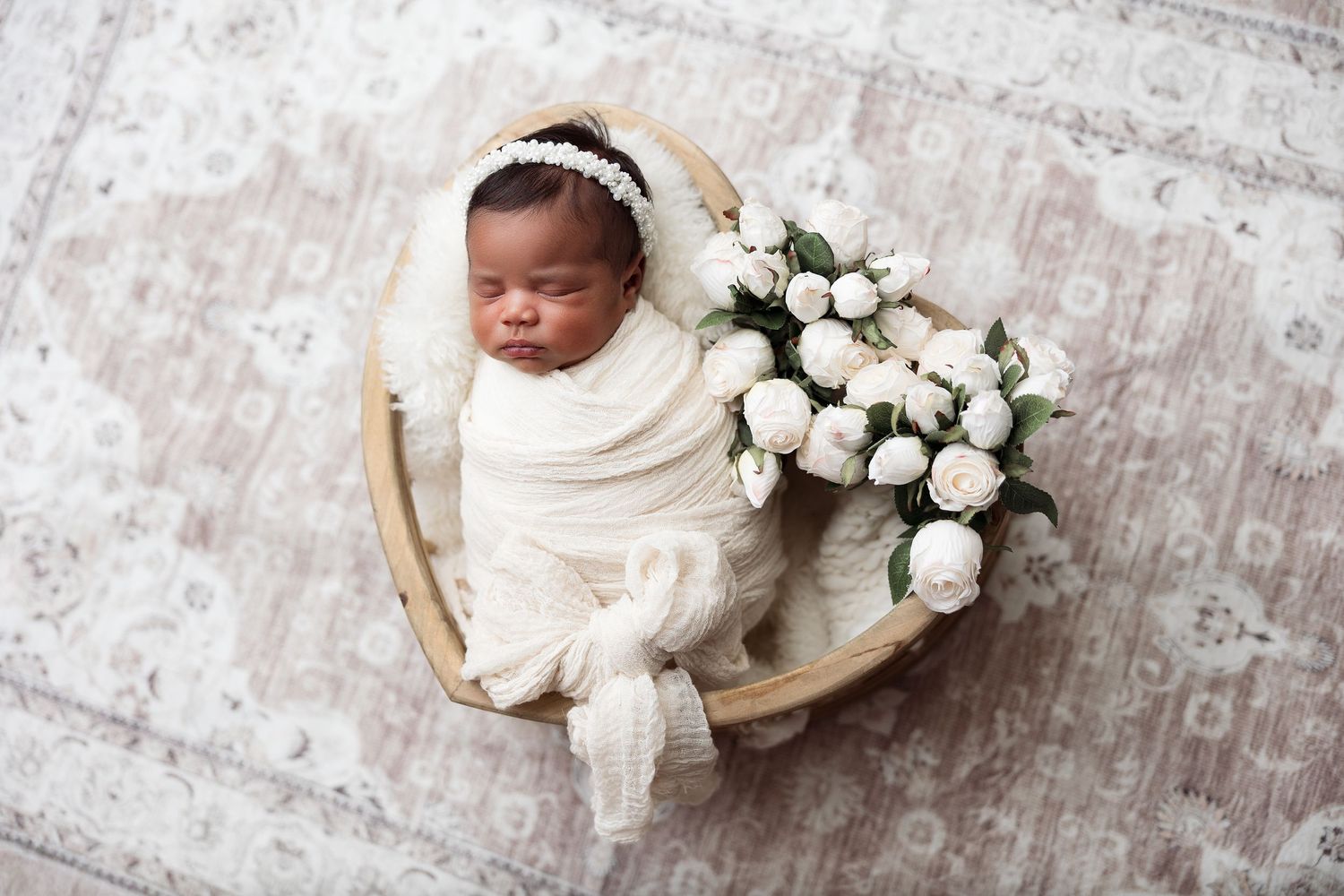 Newborn baby in basket with white roses on vintage rug.
