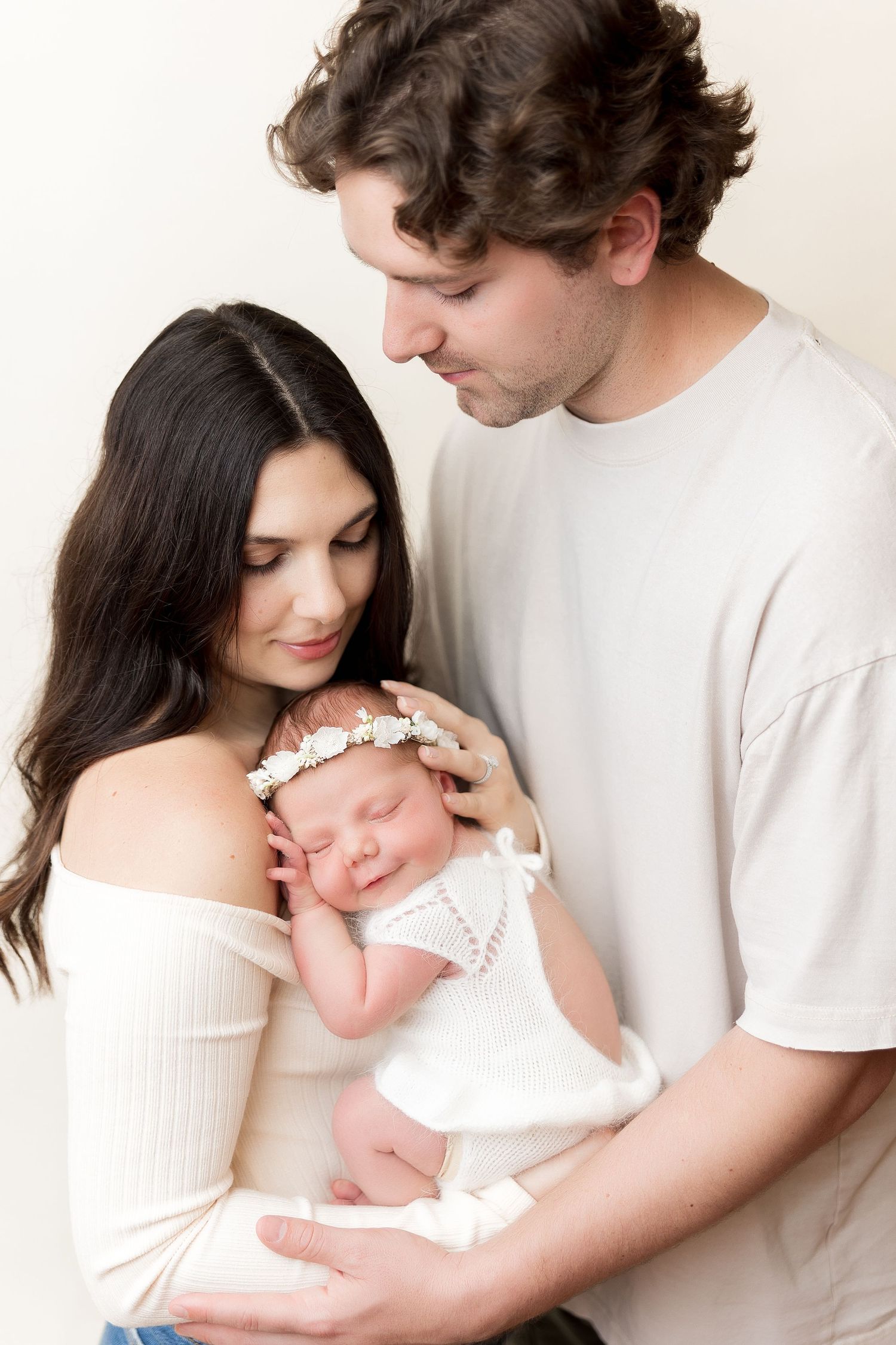 Parents gaze lovingly at their newborn baby wearing white lace headband.