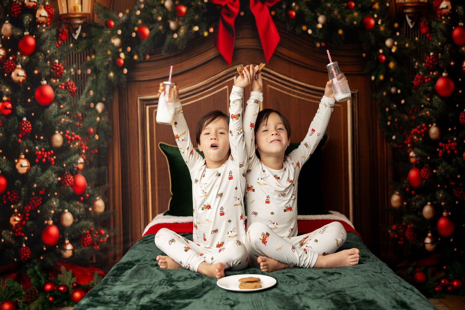 Siblings in holiday pajamas raising milk glasses beside cookies at a Christmas mini session in Pacific Grove