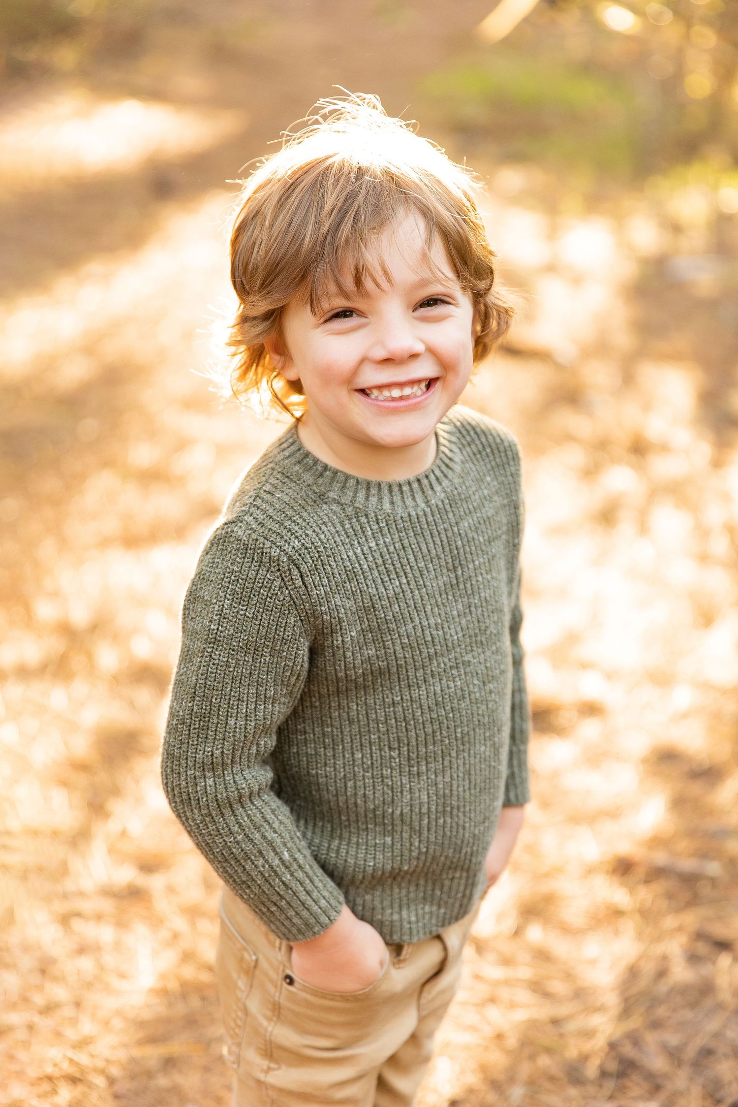 Child in green sweater smiling during golden hour photo session in nature.