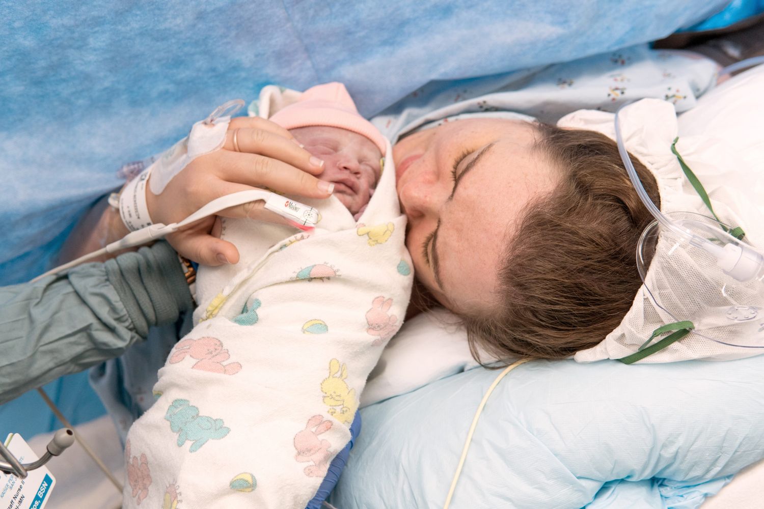 A sleeping child lies on blue bedding while holding a bottle with a colorful patterned blanket.