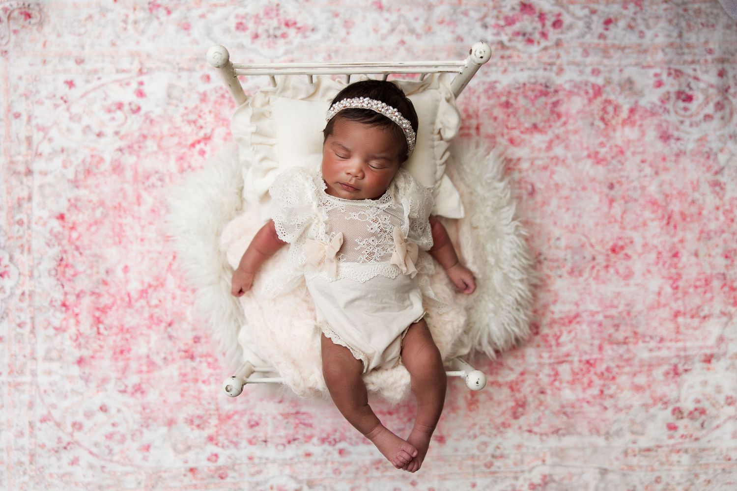 Sleeping baby in white outfit on floral pink background with plush white blanket.