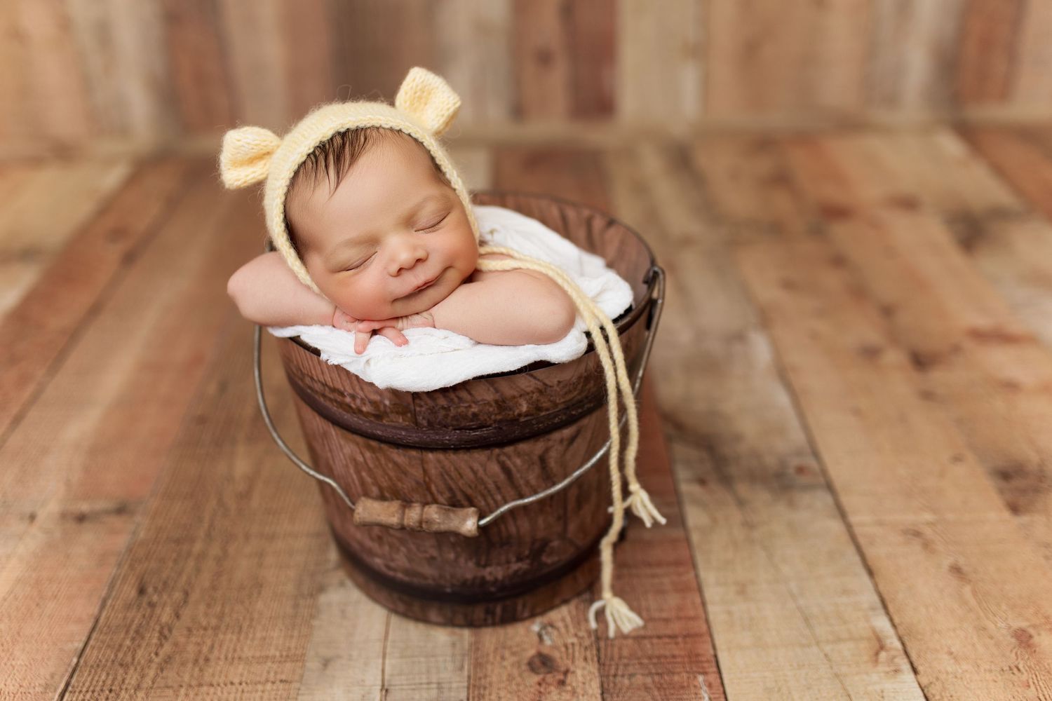 Newborn photography session with rustic wood backdrop and cozy brown blankets.