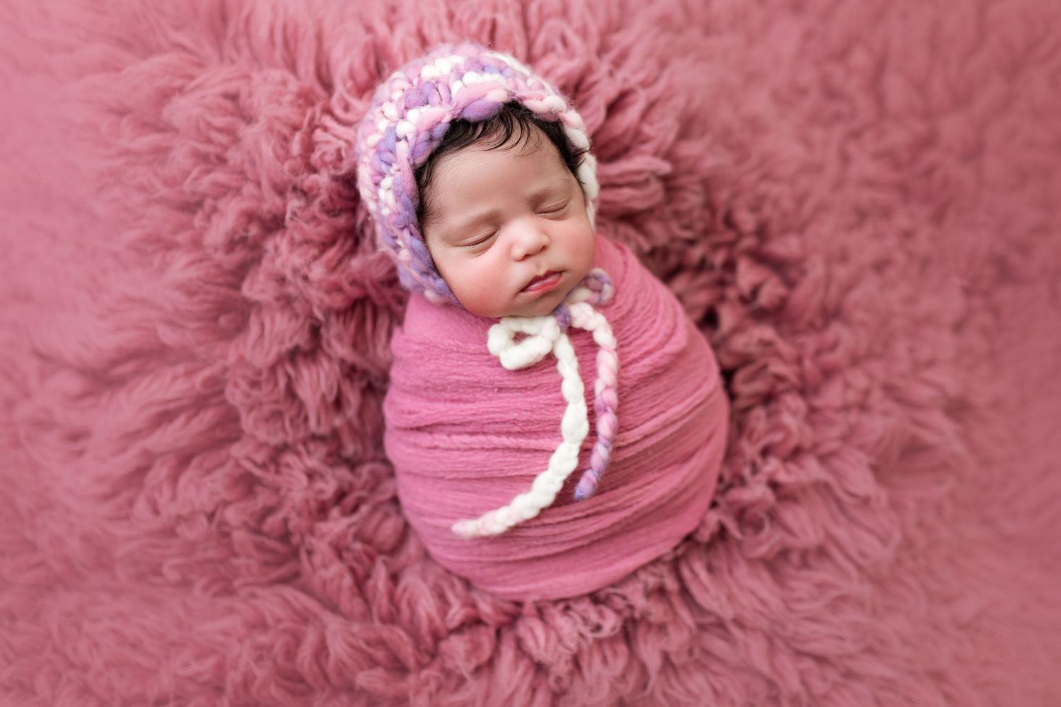Artistic newborn portraits with pink floral headpiece against rose-colored background.