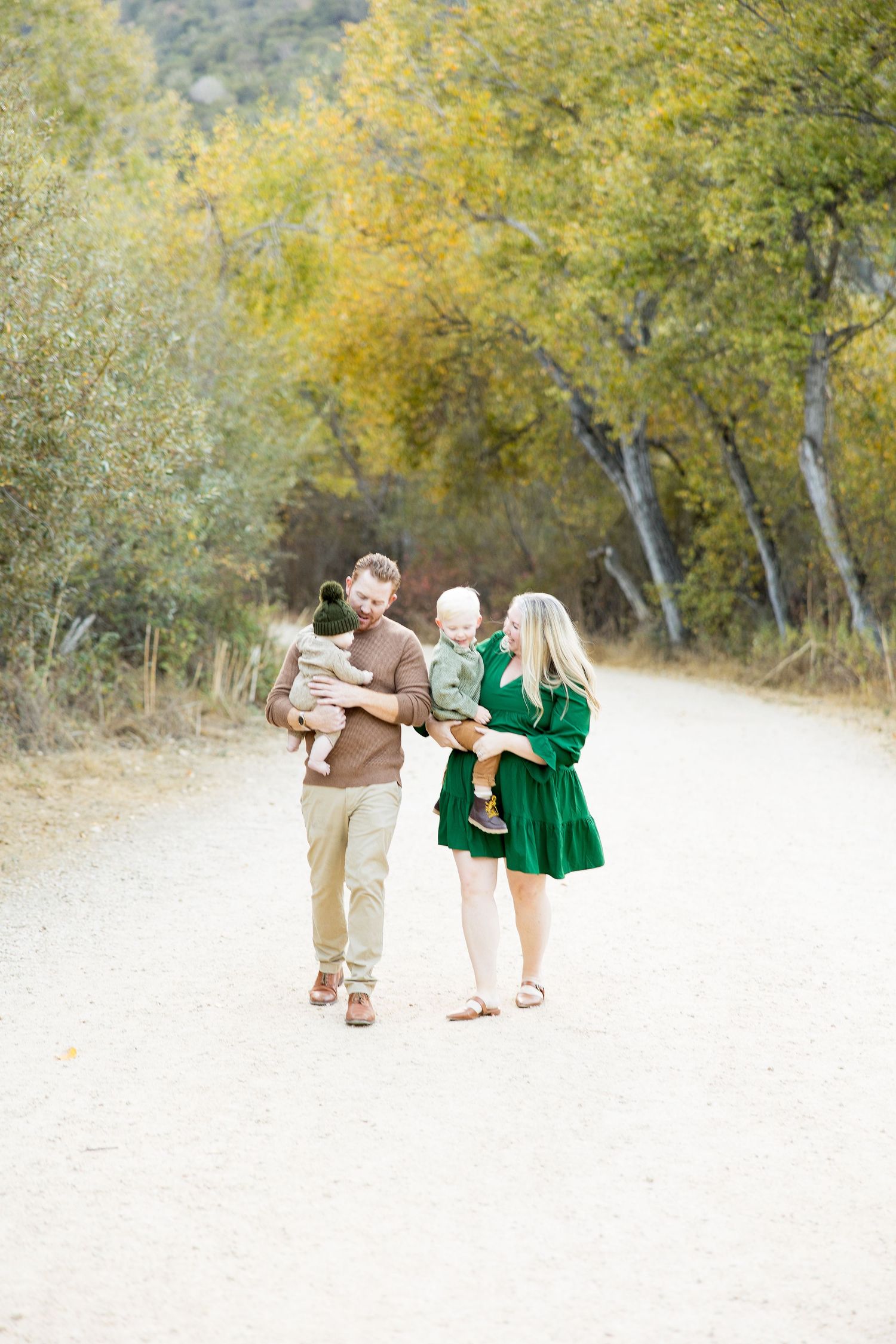 Family walking together in autumn scenery with golden light and yellow trees.