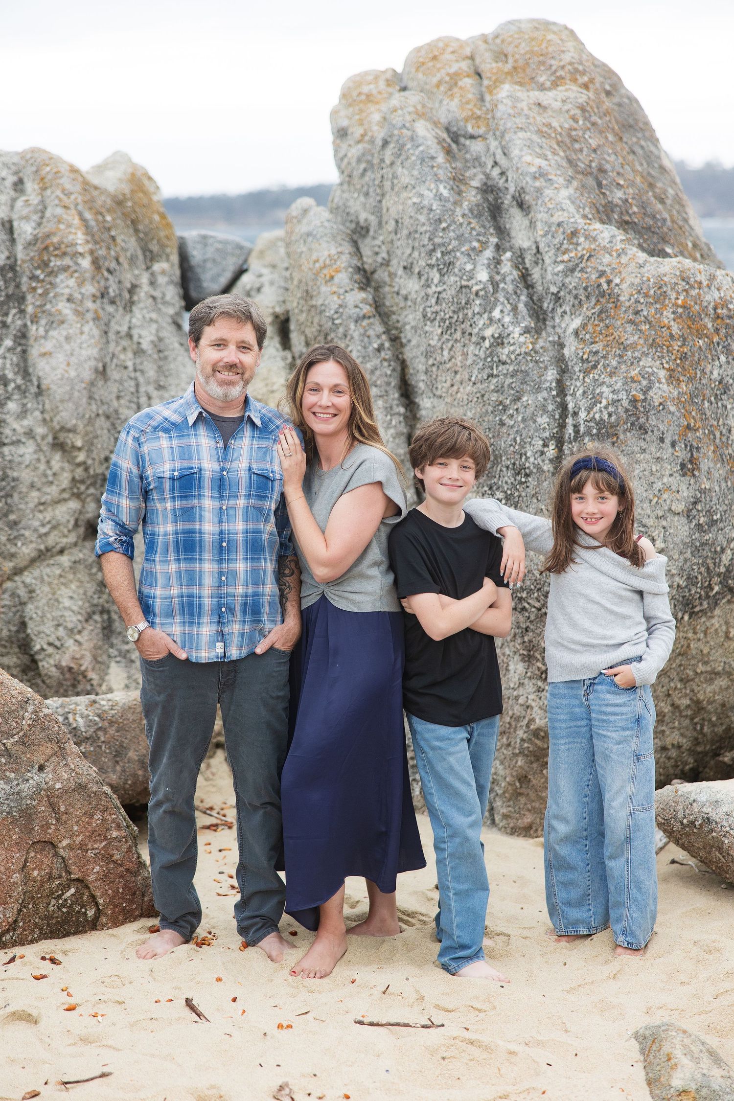 Family of four smiling together at Carmel River Beach wearing casual clothes.