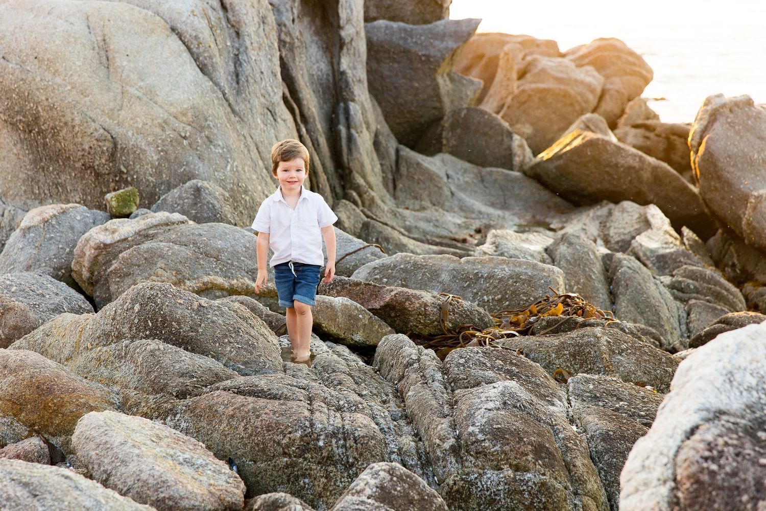 Rocky coastal landscape with large granite boulders and ocean waves at sunset.