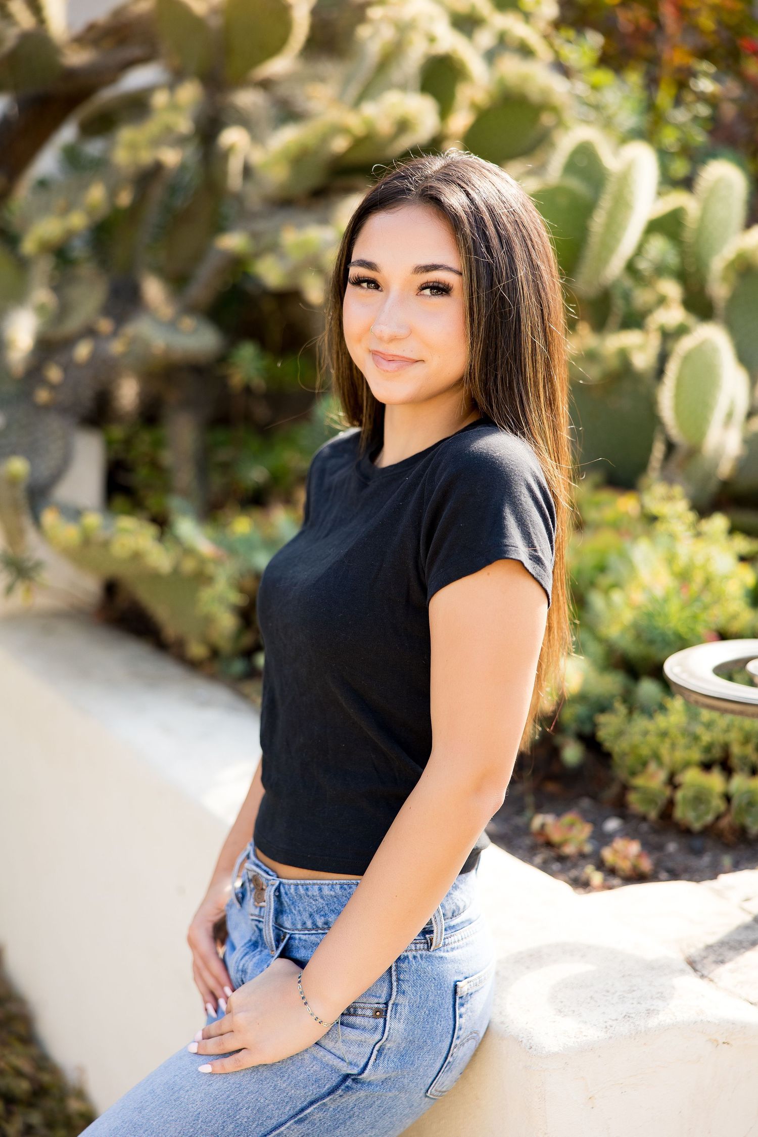 Young woman in black crop top and jeans posing beside large cactus outdoors.