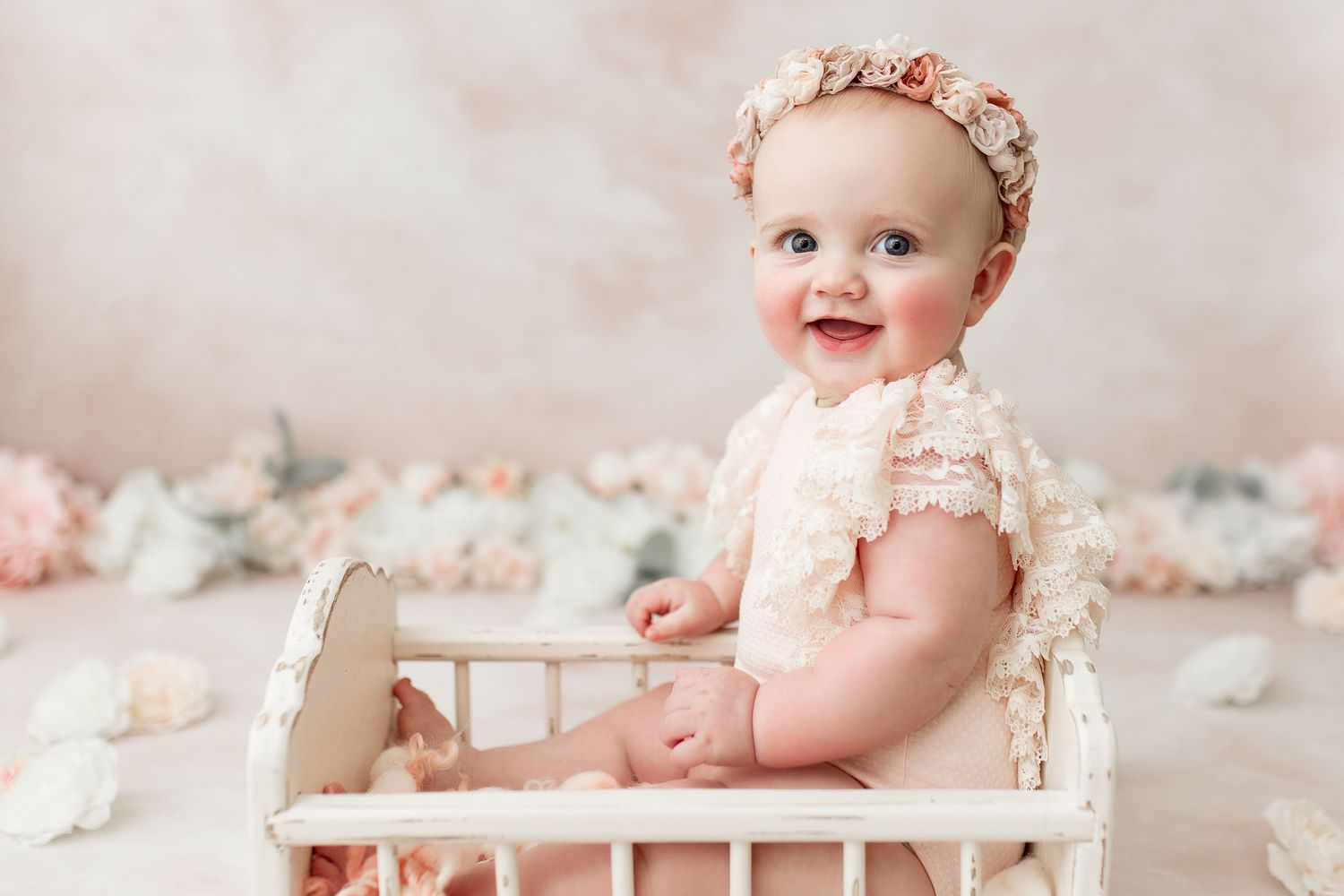 Baby in pink floral crown resting in vintage wooden bed with soft decor.