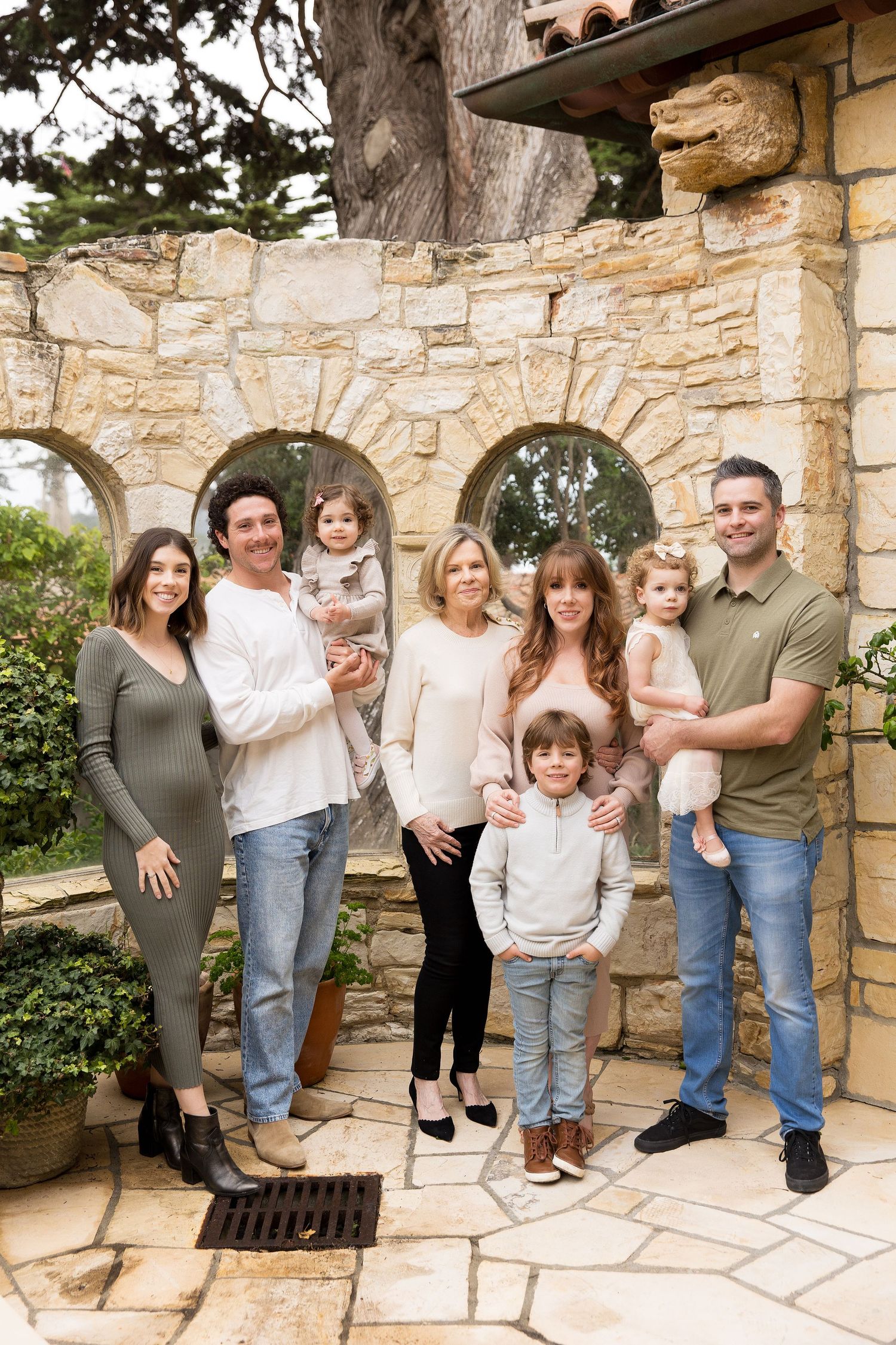 Extended family photo shoot against stone wall architecture in casual coordinated outfits, in Carmel by the Sea.