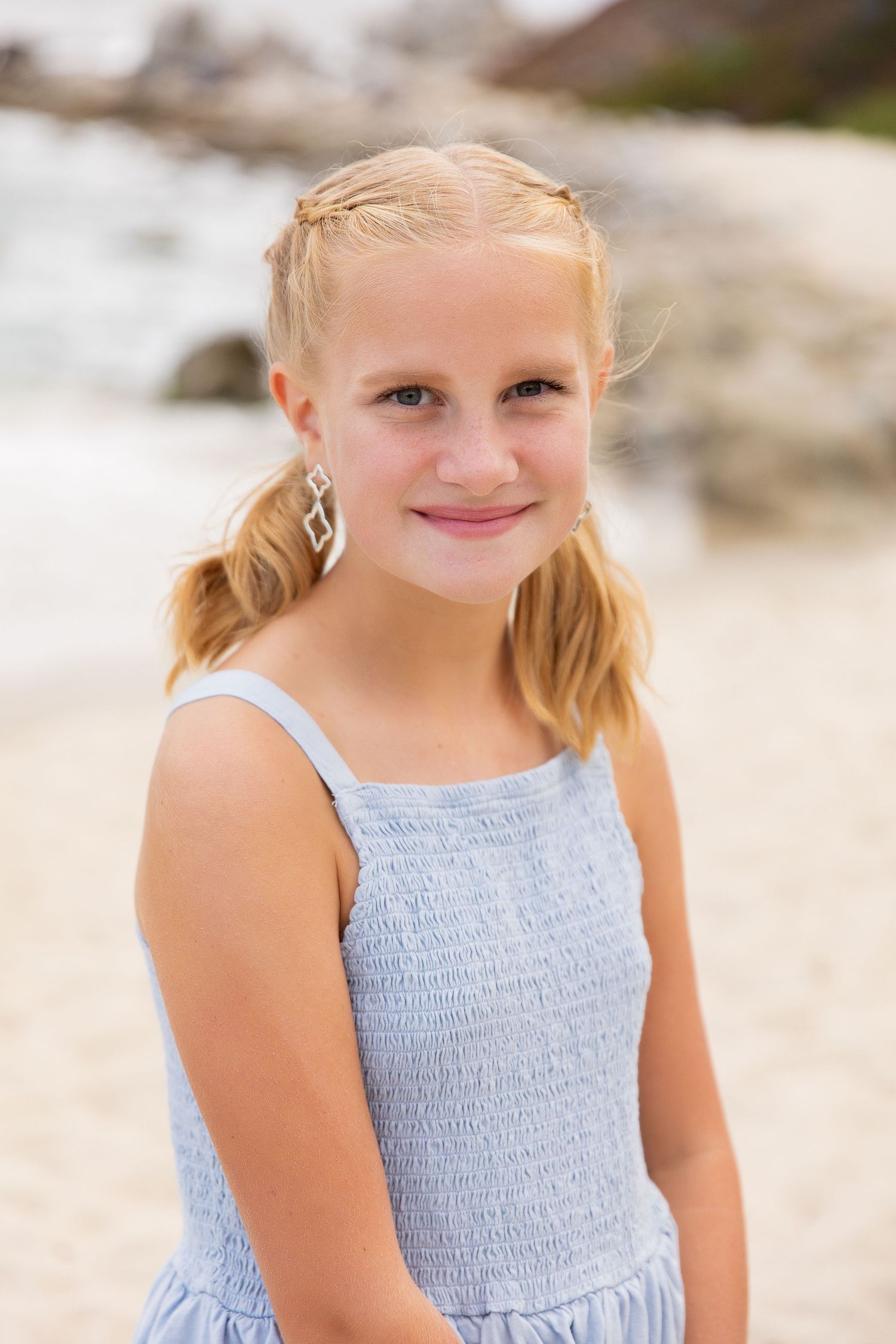 A young person in a light blue summer dress smiles at the beach.