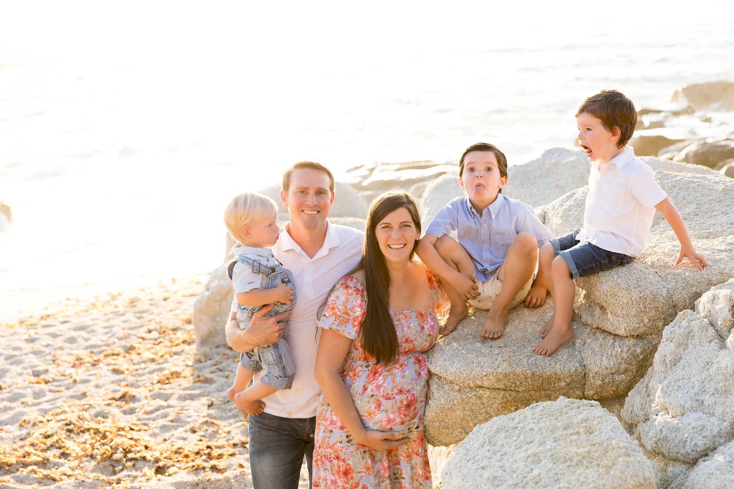 A family poses together on coastal rocks during golden hour at the beach.