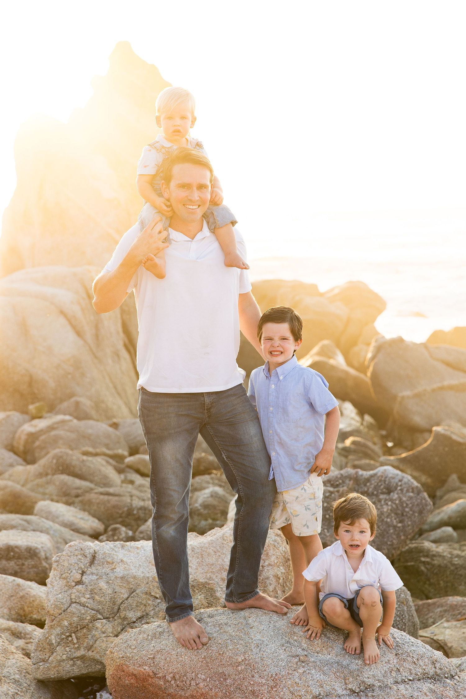 Family walking together on rocky coastal beach during golden sunset.