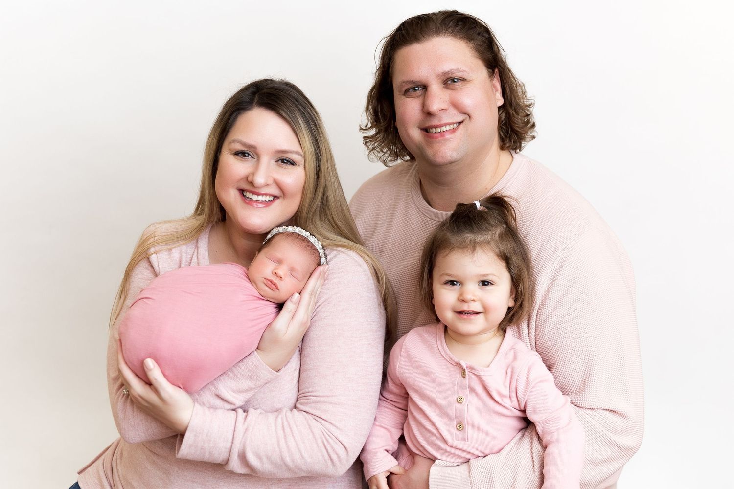Family wearing coordinated pink and white outfits poses together against white background.