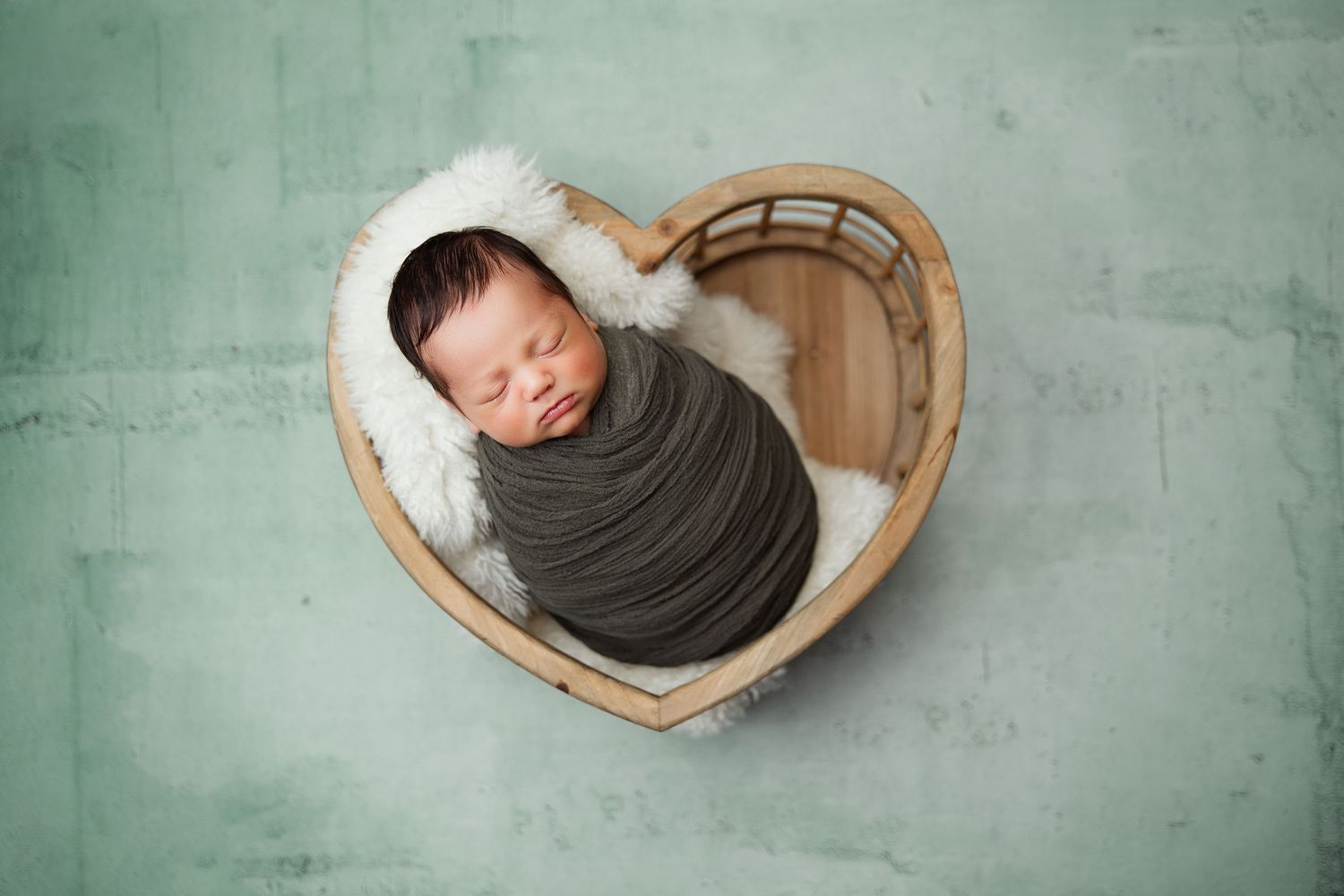 Artistic newborn photography series showing sleeping baby in curved wooden prop against green backdrop.