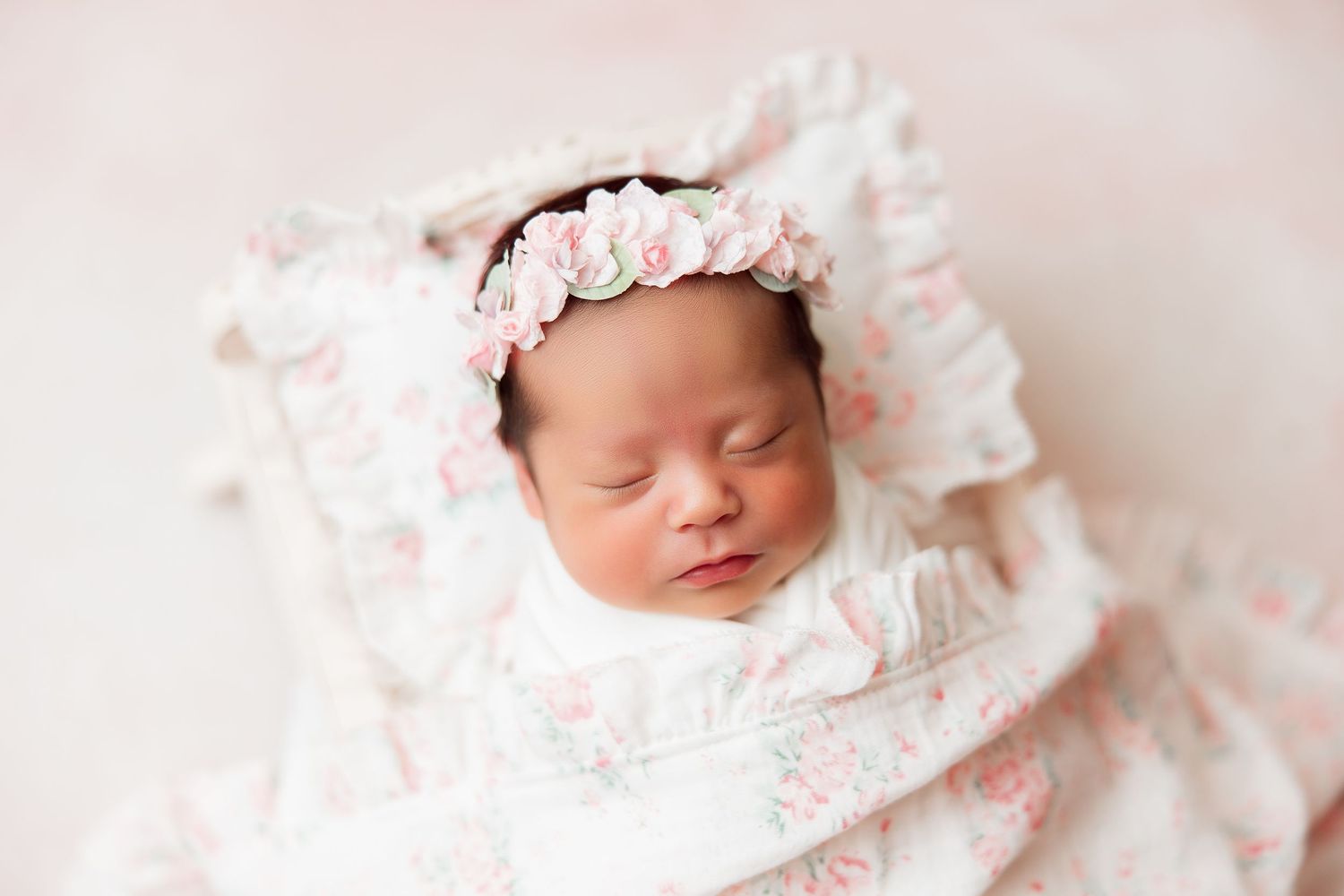 Sleeping newborn in delicate floral headband and ruffled white dress.