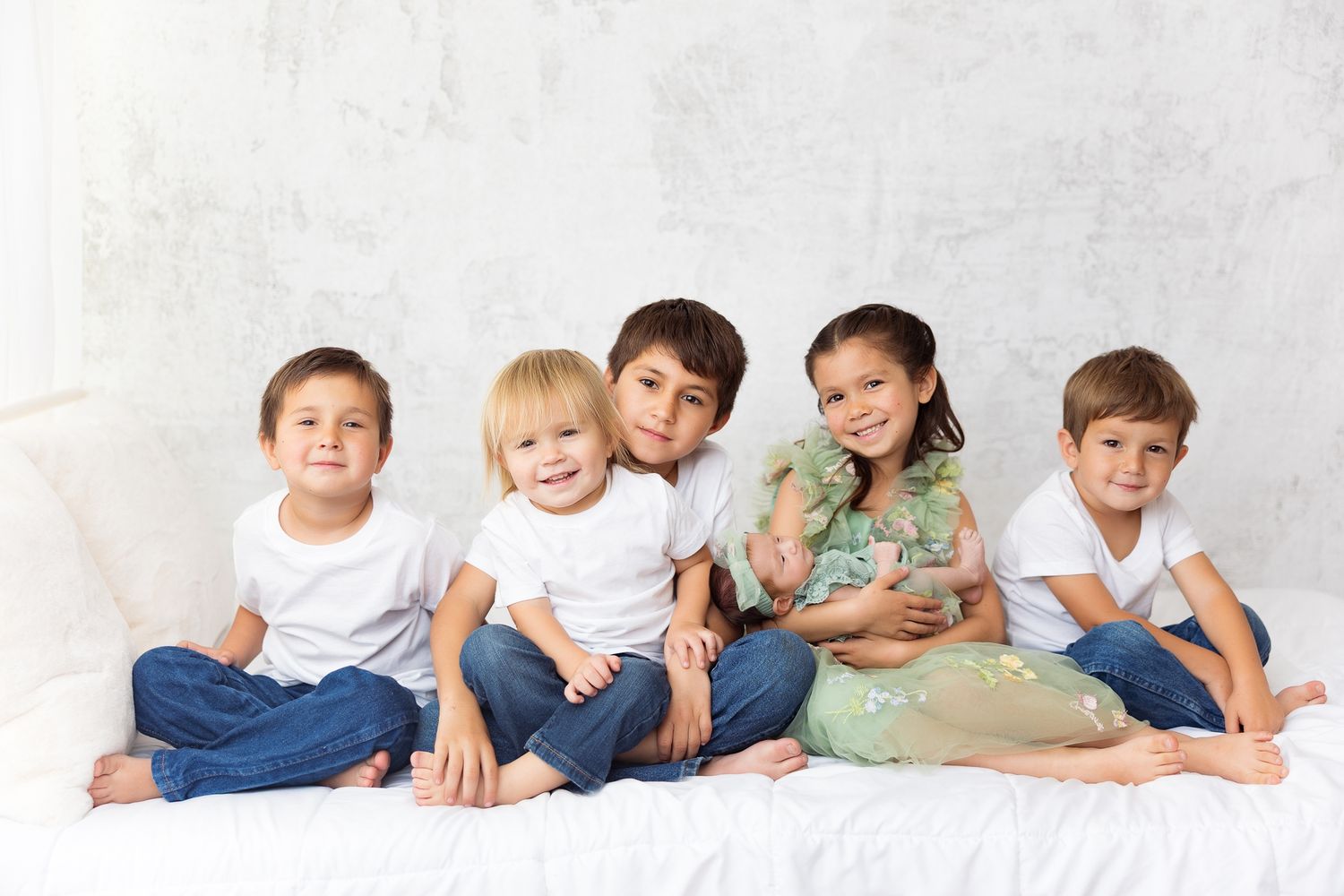 Children wearing white clothing lie in a row on a light background creating a playful and serene portrait composition.