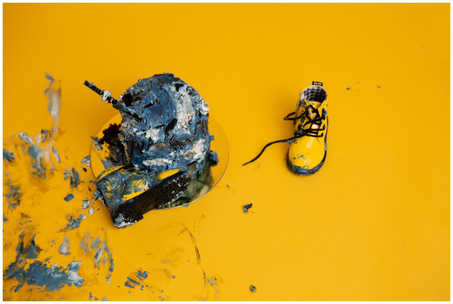 Black paint strokes and splatters create an abstract pattern against a vibrant yellow background.