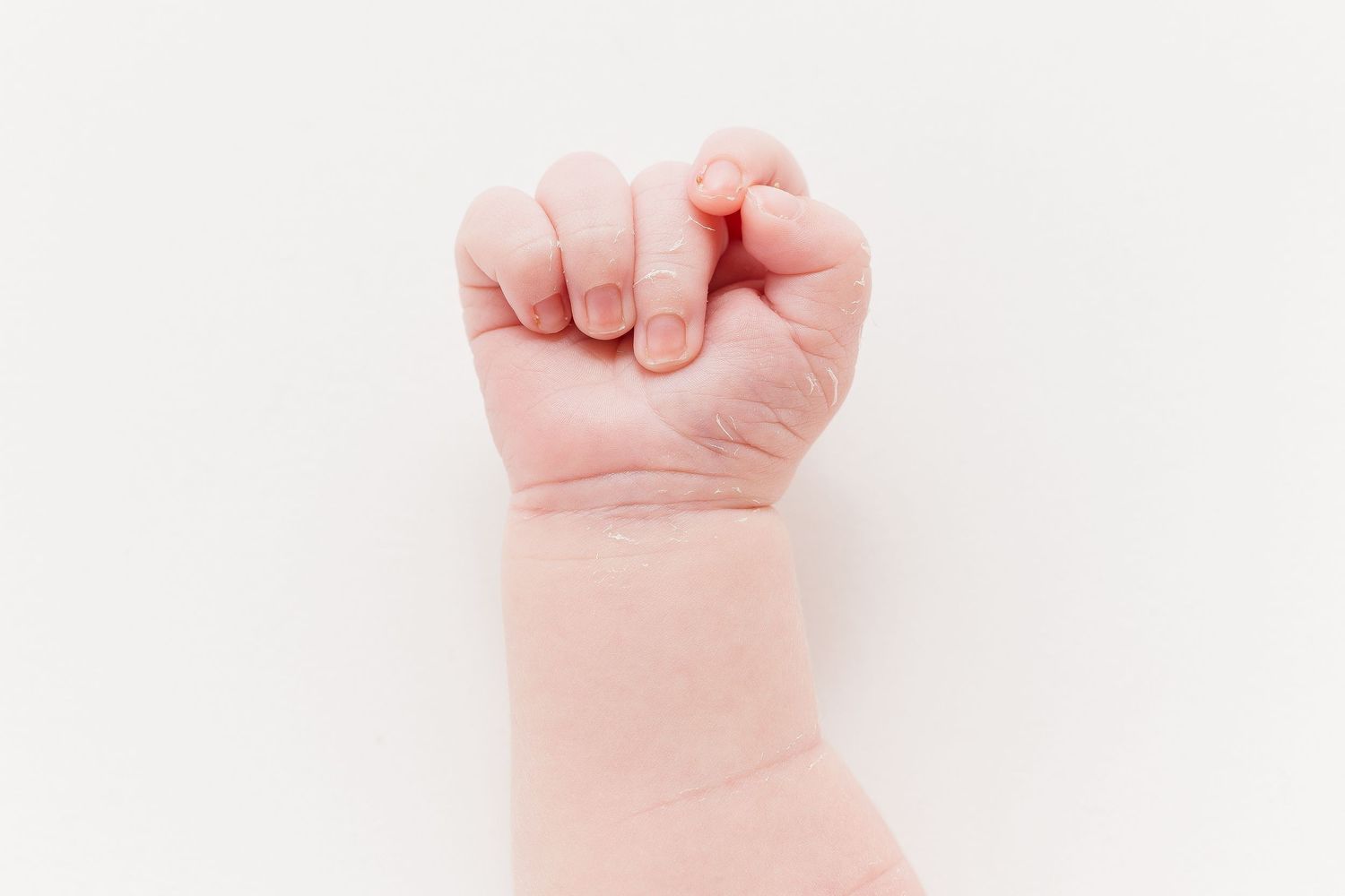 Three tiny baby fists raised up against a white background showing infant hands.