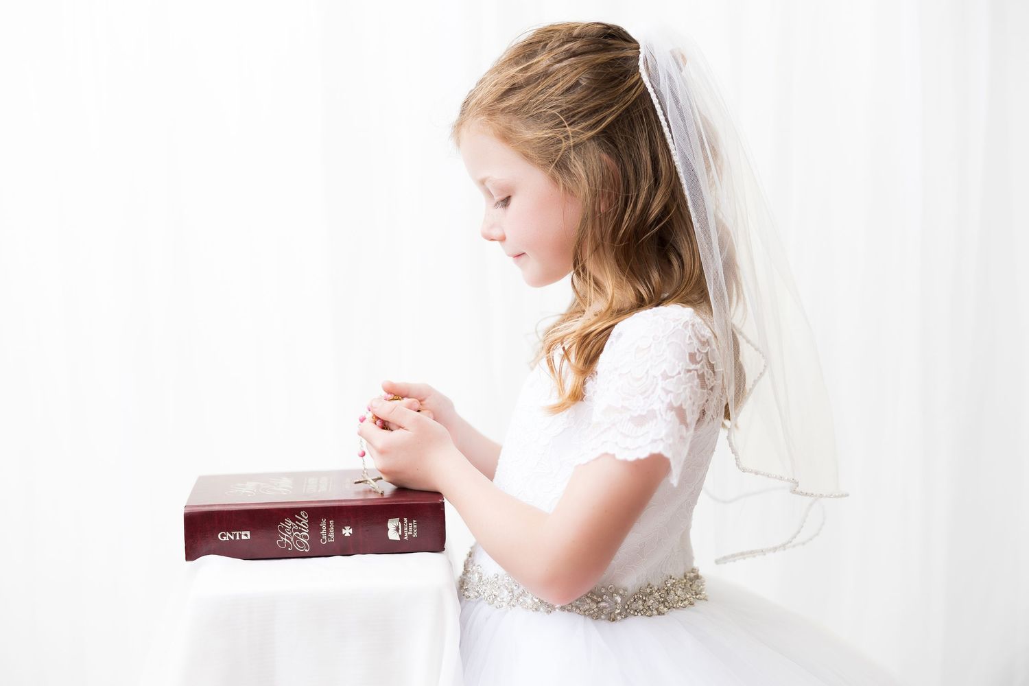 A person wearing white lies on a bed reading a book in soft natural light.