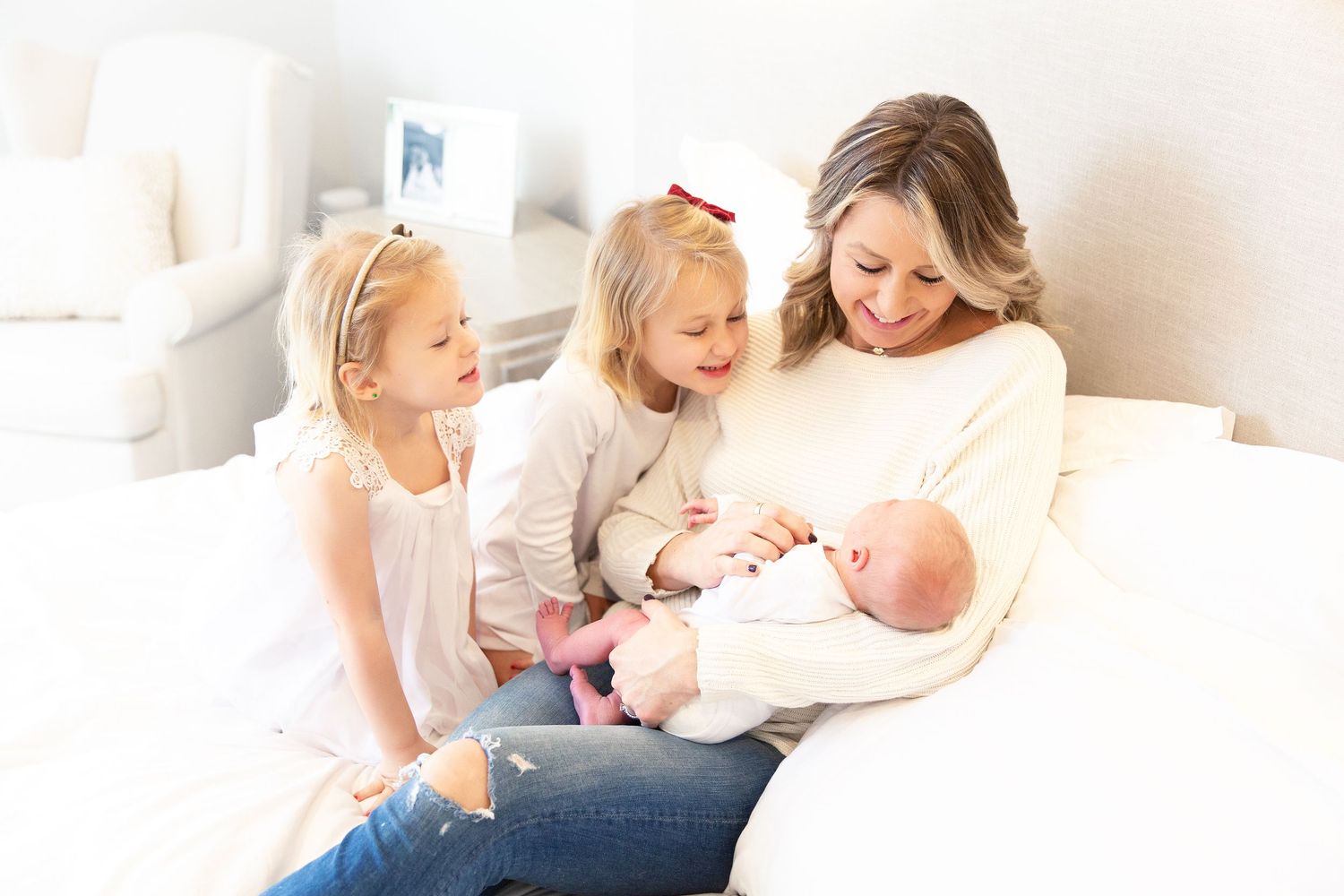 Light-filled bedroom with family members sharing intimate moments on white bedding.