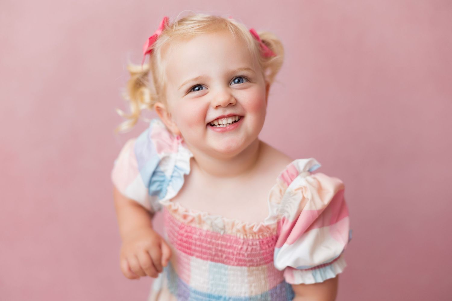 Sweet toddler in pink and blue dress smiling during studio photo session.