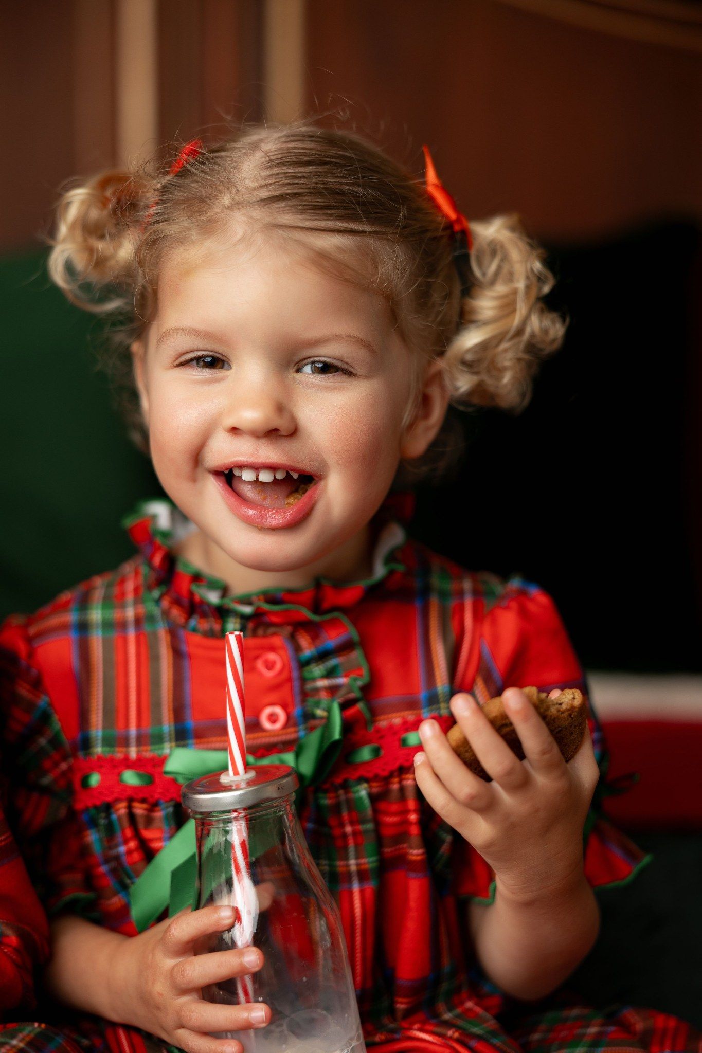 Laughing toddler in a red plaid Christmas dress with a cookie and milk jar at a Milk & Cookies holiday mini session in Pacific Grove