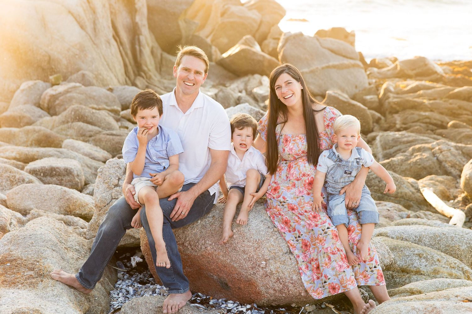 People gather on coastal rocks during golden hour as waves crash behind them at the beach.