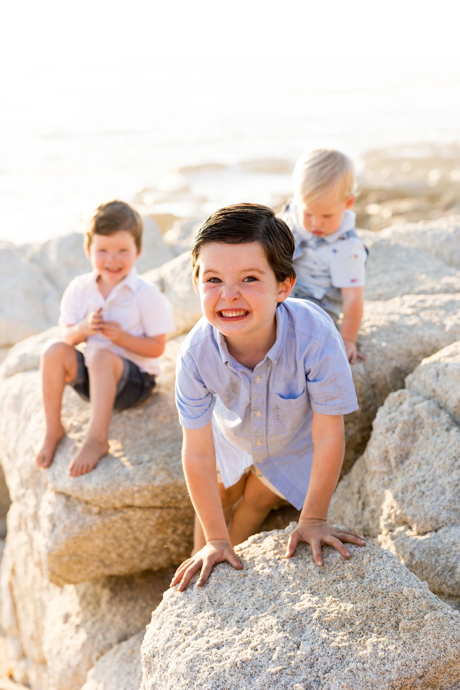 Children sitting and playing on large coastal rocks during golden hour photography session.