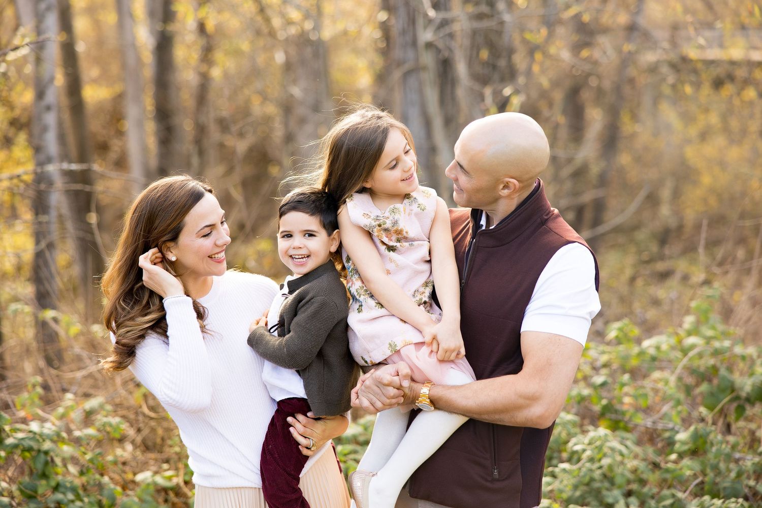 Family laughing and embracing together in autumn forest setting.