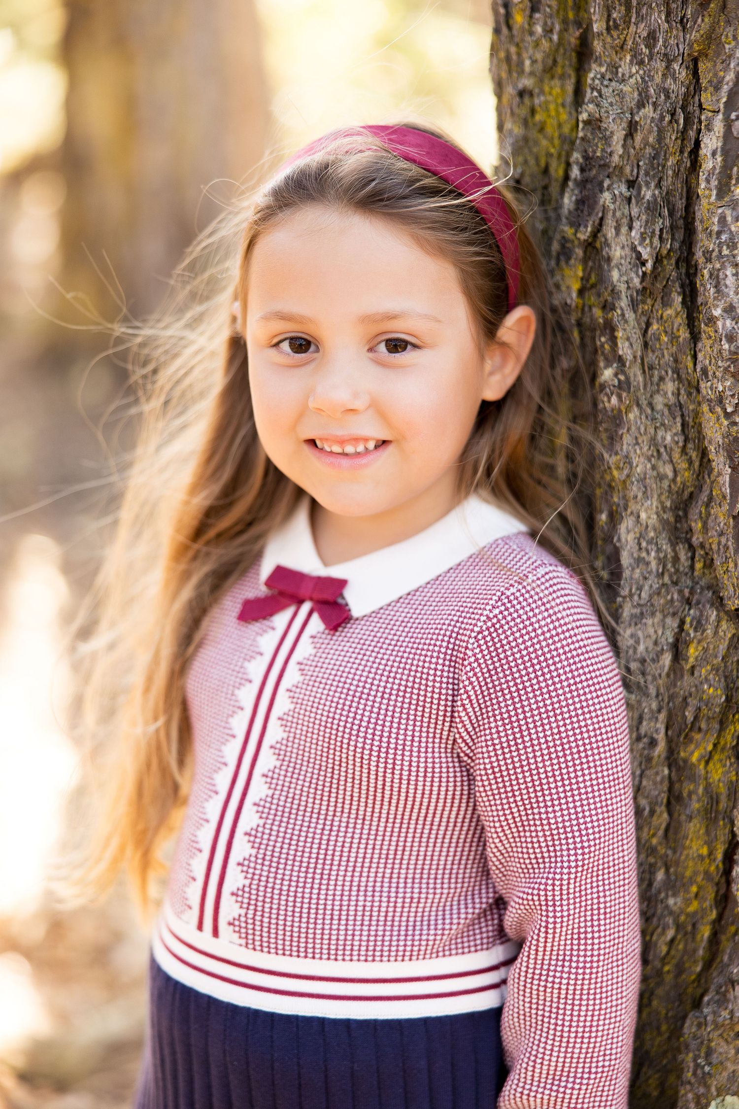 Young girl wearing a red and white checkered dress smiling against a blurred nature background.