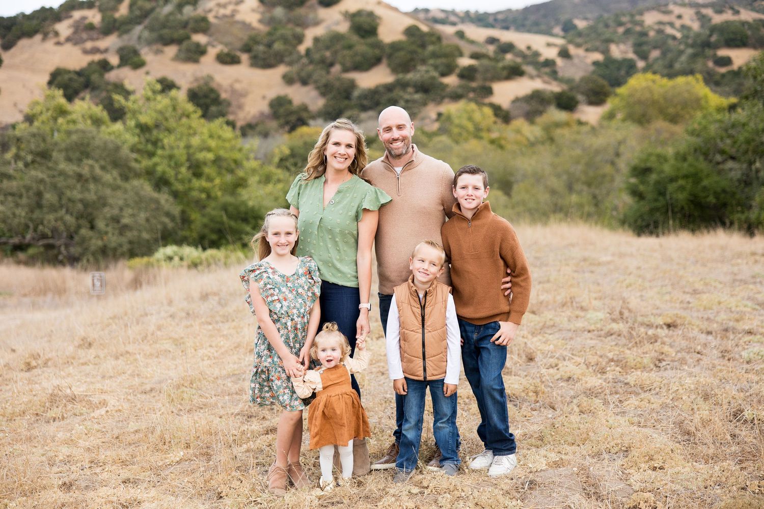 Family group poses together on a scenic hillside with rolling mountains in the background.