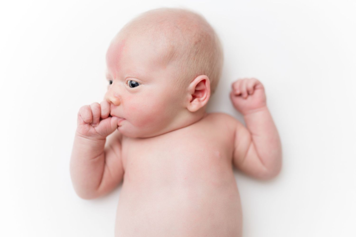 Infant laying on side against white background in minimalist style.