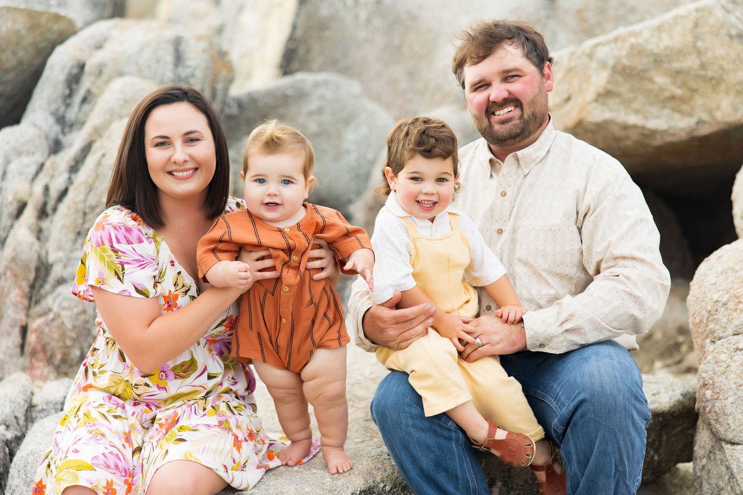 Family group portrait on rocky beach wearing coordinated casual outfits.