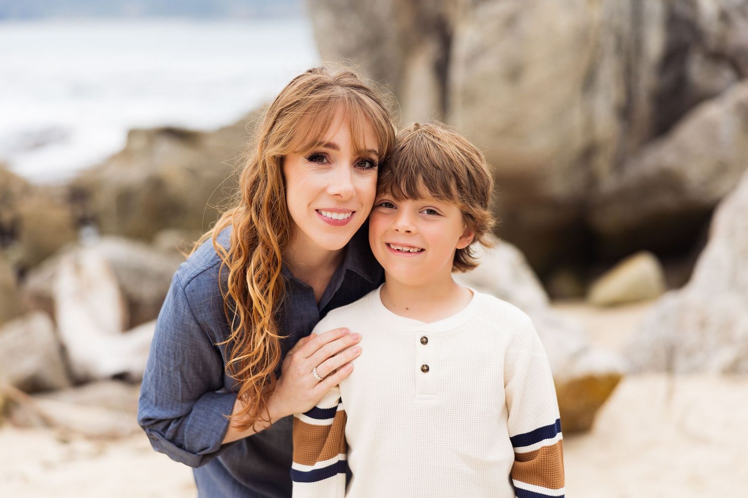 Family photo session on rocky beach with casual clothing and warm lighting.