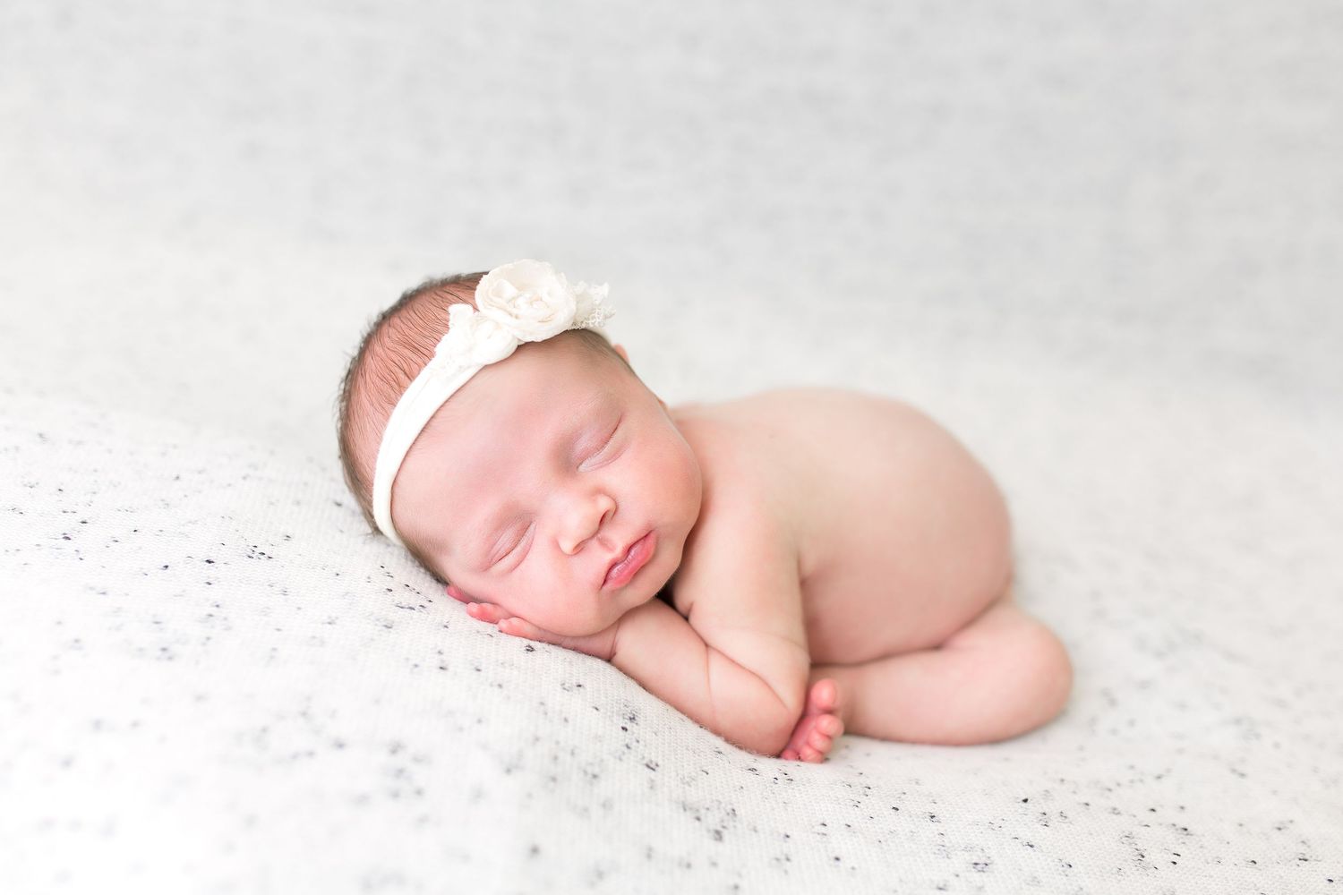 A sleeping newborn wearing a delicate headband posed on white textured backdrop.