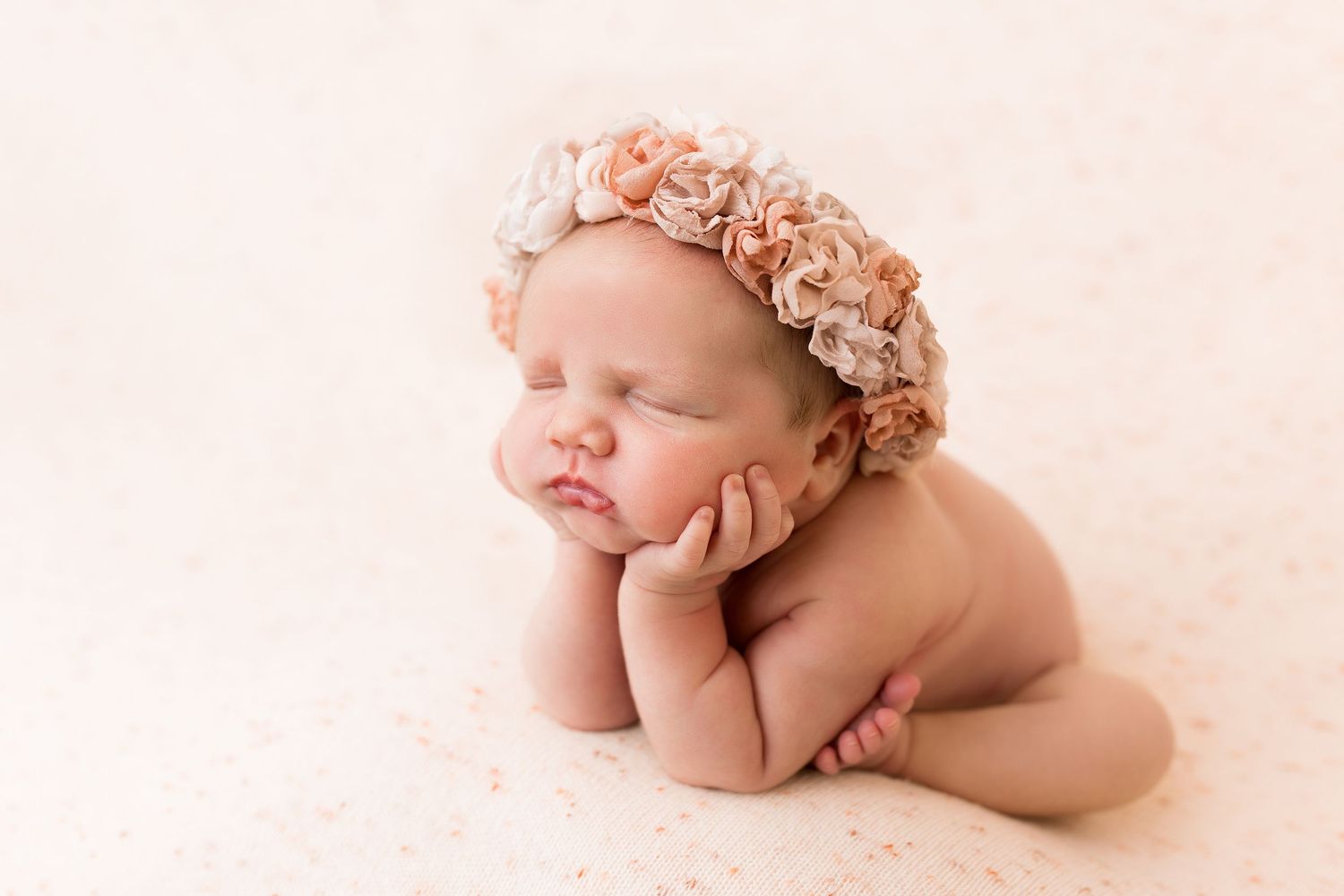 Sleeping newborn wearing peach floral crown on soft pink backdrop.