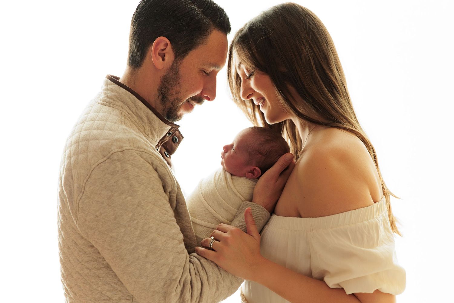 Couple in neutral tones gazes lovingly at their newborn baby.