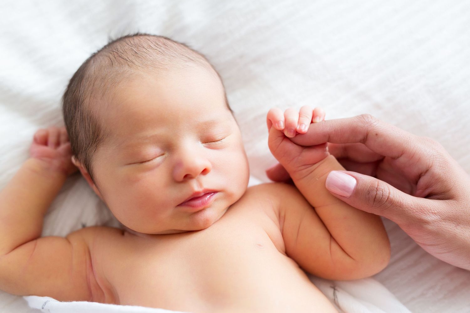 Sleeping newborn baby with soft skin lies peacefully on white fabric.