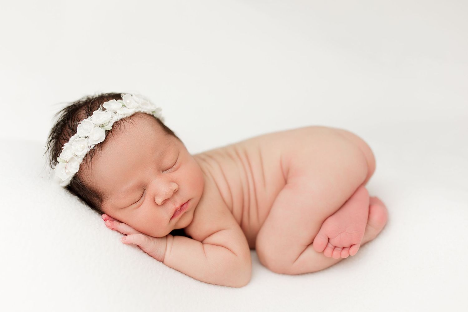 Minimalist newborn portrait with baby sleeping peacefully on white background.