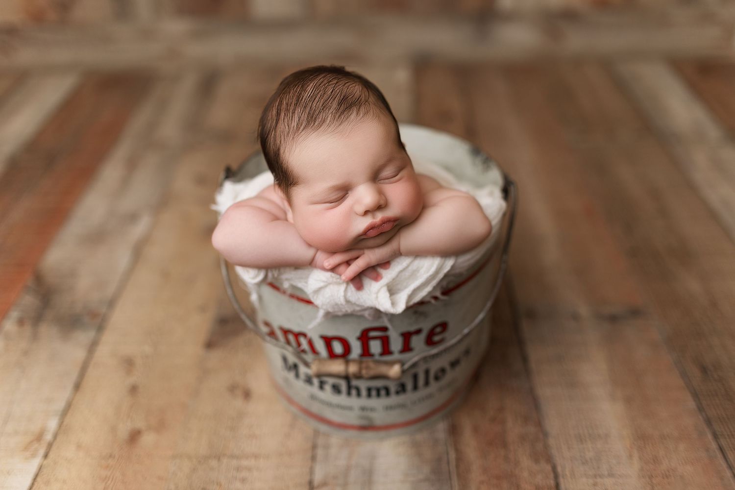 Newborn resting peacefully in vintage-style container on rustic wooden floor.